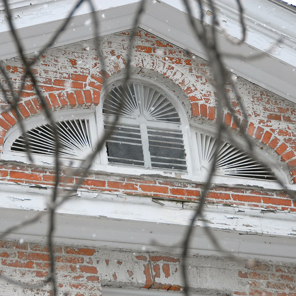 Close up view of the gable of an old briick building with flaking white paint