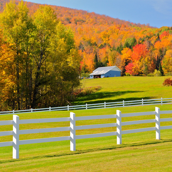 View of a Vermont farm set against mountains covered in autumn color with a horse fence in the foreground