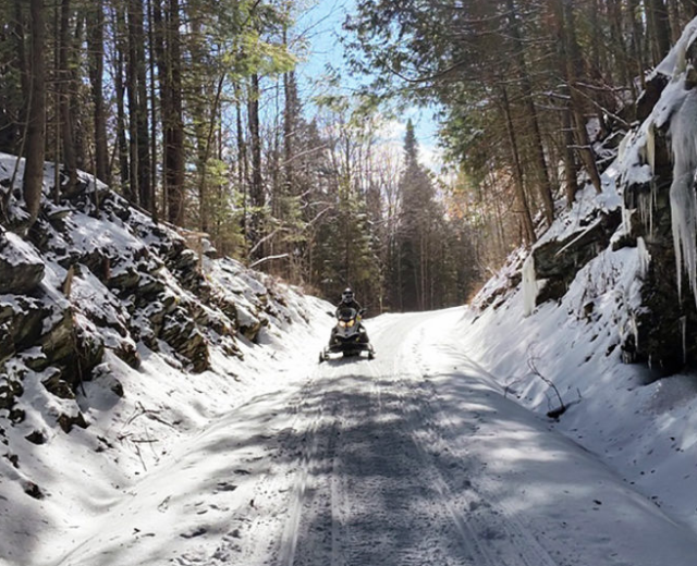 A snowmobiler on a Vermont trail in the woods during winter