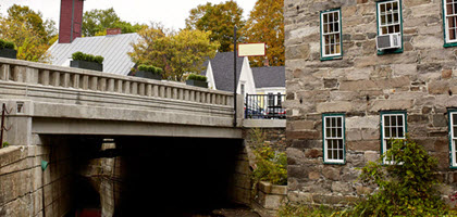 Daytime view of a bridge iover a creek next to an old stone building