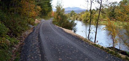 Daytime view of a trail paved over a railroad right of way next to a river