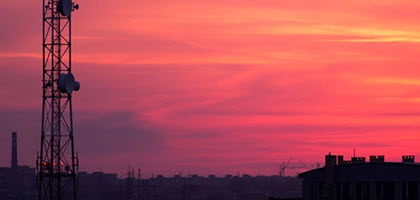 Sunset view of a radio tower with a city skyline silhouetted in the distance